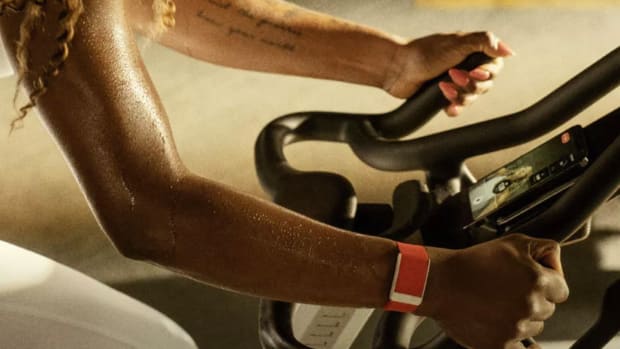 A woman using the WHOOP 4.0 app and wristband while exercising on a spin bike